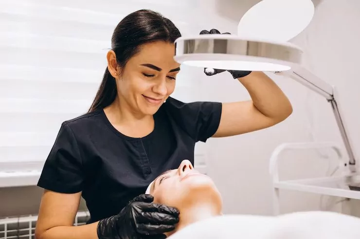 Chuyên viên kiểm tra da mặt khách hàng dưới đèn lúp.